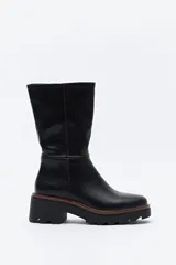 Bota de caña media en cuero sintético color negro, con diseño minimalista y suela robusta dentada con detalle de borde en color marrón.