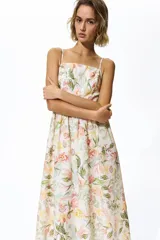 Vestido midi de color crudo con estampado floreado en tonos pastel, escote cuadrado y tirantes finos. Presenta un diseño ajustado en el torso con corte en la cintura y falda fluida con vuelo.