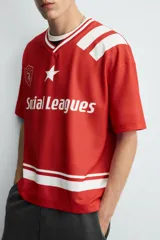 Camiseta de manga corta color rojo, corte boxy fit, con cuello pico ribeteado en blanco. Presenta un estampado frontal con el texto "Social Leagues", una estrella blanca y un escudo con el número "4". Tiene detalles de franjas blancas en el bajo y en los hombros.