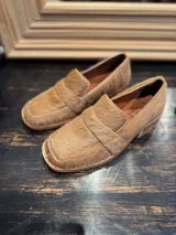 Mocasín de punta cuadrada confeccionado en piel con textura de pelo, color beige tostado, con detalle de antifaz en el empeine y costuras visibles en el borde.