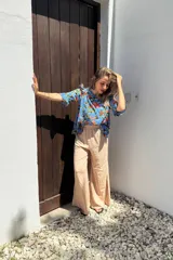 Blusa celeste con estampado floral en tonos naranja, verde y marrón. Tiene escote redondo y mangas cortas con volados.