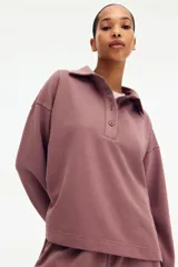 Buzo en tejido liviano color malva con cuello camisero, tapeta de botones, hombros caídos y puños acanalados.