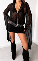 Vestido corto negro de estilo lencero con escote en V profundo, mangas largas acampanadas de tul transparente y diseño ajustado al cuerpo.
