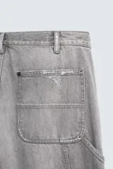 Pantalón de jean estilo carpintero con corte relaxed fit, tiro medio y pierna recta. Presenta un lavado azul medio con efecto desgastado y roturas en las rodillas. Incluye bolsillos laterales tipo plastrón, tira multifunción en la pierna, cierre frontal con cremallera y botón.