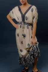 Vestido largo beige con estampado paisley en color azul marino, escote en V profundo con detalle bordado, mangas cortas amplias, cordón ajustable en la cintura con borlas y volados en el ruedo.