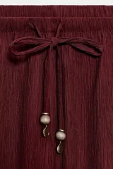 Pantalón de tiro medio y pernera recta con textura, de color marrón. Cuenta con cintura elástica y cordón ajustable con abalorios decorativos.