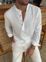 Camisa de lino blanca con cuello mao y cierre frontal parcial con botones de madera. Presenta mangas largas con detalle de trabilla para arremangar.