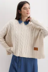 Sweater de punto con diseño de trenzas verticales, corte crop y holgado. Presenta mangas largas y un parche de cuero sintético con el logo de la marca en la parte inferior.