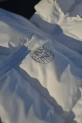 Campera puffer blanca con capucha y logo reflectivo en el pecho.