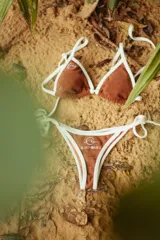 Conjunto de bikini marrón con detalles en blanco, compuesto por un corpiño triangular con tirantes finos y una bombacha con tiras laterales ajustables.