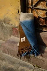 Bufanda tipo manta suave con diseño de bloques de color en tonos beige, azul y marrón, terminada con flecos en los extremos.