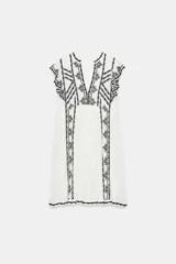 Vestido corto blanco de Zara Woman Collection con bordados en contraste de color negro, escote en V y mangas sisa con pequeños volados.