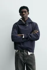 Sudadera de calce relajado color azul marino, con cuello alto y cierre frontal mediante alamares metálicos. Presenta manga larga y terminaciones en rib en puños y cintura.