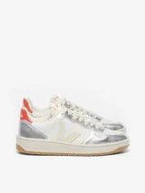 Championes Veja modelo V-10, con diseño de paneles en cuero blanco y cuero metalizado plateado. Presentan el logo lateral en color crema, detalle de talón en color rojo con la marca estampada y suela de caucho color caramelo.