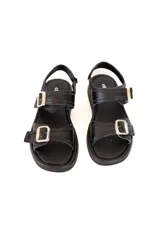 Sandalia de cuero negro con plataforma baja, diseño de dos correas ajustables con hebillas metálicas doradas y tira trasera con cierre de velcro.
