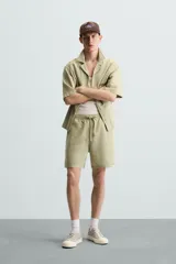 Bermuda de algodón color blanco, de corte relajado (relaxed fit), con cintura elástica ajustable mediante cordón. Posee bolsillos laterales y un bolsillo trasero de plastrón. Presenta un bordado en contraste en la pernera.