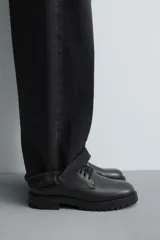 Bota tipo derby de cuero negro con cordones al tono, horma redonda y suela track con ligero tacón.