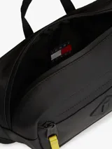 Ri±onera negra Tommy Jeans de diseño urbano, confeccionada en poliuretano y poliéster. Cuenta con un compartimento principal, bolsillo exterior con cierre de cremallera, tiradores en color amarillo, asa superior, correa ajustable y el parche bordado con el logotipo de la marca.