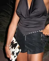 Short negro de cuero sintético de tiro bajo con cierre frontal y tres correas decorativas con hebillas metálicas en el lateral.