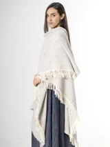 Ruana de punto color beige con sutiles motas multicolores, con bordes terminados en flecos largos.