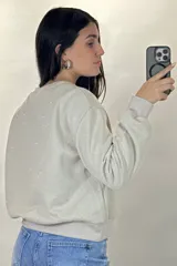 Buzo de cuello redondo y manga larga, color negro, con diseño de pequeños puntos brillantes distribuidos por toda la prenda. Presenta puños y ruedo acanalados.