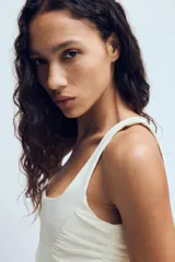 Top estilo corset de color blanco con escote cuadrado y tirantes anchos. Presenta paneles laterales y centrales con tejido drapeado, estructura entallada y cierre posterior con cremallera.