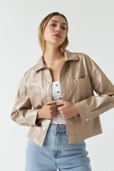 Chaqueta color beige de cuero sintético con cuello clásico, cierre frontal con botones, bolsillos tipo parche en el pecho y corte holgado.