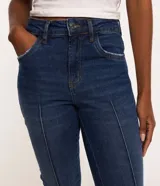 Pantalón de jean skinny azul oscuro con trabillas en la cintura, cierre tradicional por botón y cremallera, bolsillos delanteros y traseros deshilachados y costuras verticales.