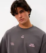 Remera gris oscuro de corte oversized con cuello redondo y manga corta. Cuenta con estampa frontal en color rosado con texto "LEAD THE WAY", tres estrellas y grafismo de números.