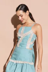 Top corto color turquesa con tirantes finos y detalles de volantes brillantes en color beige que forman un patrón geométrico en el frente.