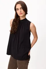 Blusa sin mangas color crema, con cuello alto fruncido y diseño holgado.