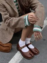 Zapato tipo guillermina de cuero color marrón, con diseño de punta dividida (split-toe), cierre con hebilla metálica y suela plana.