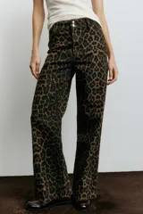 Pantalón de jean de tiro alto con pierna amplia y corte holgado, confeccionado en tela con estampado de leopardo en tonos marrón y negro. Presenta cierre y dos botones dorados en la cintura, y pliegues frontales.