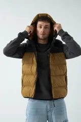 Chaleco marrón con capucha y cuello alto, con cierre frontal y bolsillos laterales. Diseño color block con parte superior negra.