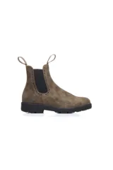 Bota tipo chelsea de cuero rústico color marrón, con paneles elásticos laterales y detalles de perforaciones estilo brogue. Cuenta con suela de goma resistente y tiradores en la parte superior de la caña.