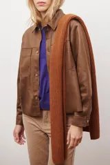Chaqueta color camel con cuello camisero, cierre frontal con botones dorados, dos bolsillos de parche en el pecho y costuras decorativas en contraste.