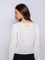 Camisa blanca de manga larga con escote en V y botones nacarados en la parte frontal.