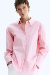 Camisa oversized a rayas color rosado y blanco, con cuello clásico, cierre frontal de botones, un bolsillo aplicado en el pecho y mangas largas con puños abotonados.