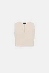 Top color crudo de tejido de punto con escote barco, manga sisa y abertura con abalorio en el centro.