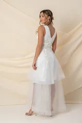 Vestido corto de tul color marfil con diseño asimétrico tipo high-low, escote en V y sin mangas. Presenta delicadas incrustaciones de flores y hojas bordadas en hilo de seda en la parte superior.