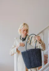 Cartera tipo tote de gamuza color marrón, con correas trenzadas y detalle de piedras naturales incrustadas en líneas verticales. Cuenta con cierre metálico y forro interior de tela.