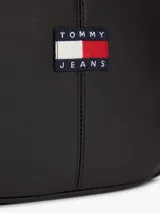 Bandolera reporter de poliuretano negro, con cierre de cremallera, correa ajustable y parche con el logo de Tommy Jeans en la parte delantera.
