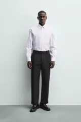 Camisa de corte regular fit con cuello italiano y manga larga con puños abotonados. Presenta un diseño de rayas verticales finas en tono suave sobre fondo claro, con cierre frontal de botones.