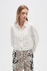Chaqueta cropped de manga larga, color blanco con finas rayas verticales en tono claro. Presenta cuello camisa, cierre frontal con botones de madera y dos bolsillos delanteros con tapa a la altura del pecho.