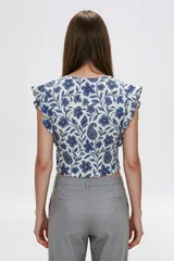 Blusa de diseño estampado con motivos florales y cachemira en tonos marrones sobre base blanca, con escote en V profundo y doble lazo frontal ajustable. Presenta mangas cortas con volados.
