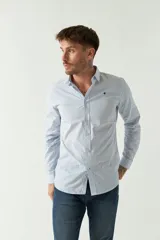 Camisa de hombre de corte slim fit, confeccionada en algodón con diseño de rayas verticales finas en tonos claros. Presenta cuello clásico, cierre frontal con botones y logo bordado en el pecho.