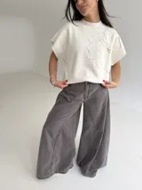 Chaleco tejido de punto color crudo, con cuello redondo y diseño de flor en relieve en el frente. Presenta un corte holgado y mangas cortas con terminación acanalada.