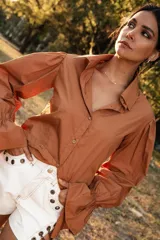 Camisa color camel con botones de madera, cuello camisero, mangas abuchonadas con puños elásticos y silueta relajada.