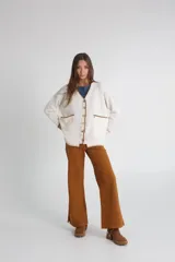 Cárdigan tejido color crudo con cuello en V, cierre con botones y bolsillos frontales con ribete en marrón.