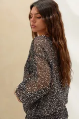 Sweater negro semitransparente de punto con aplicación de lentejuelas plateadas brillantes, cuello redondo y mangas largas holgadas.